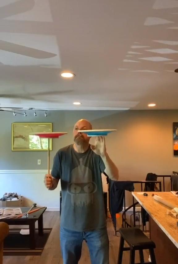 Guy Juggles Two Spinning Plates Between Stick in one Hand and Finger of Other Hand