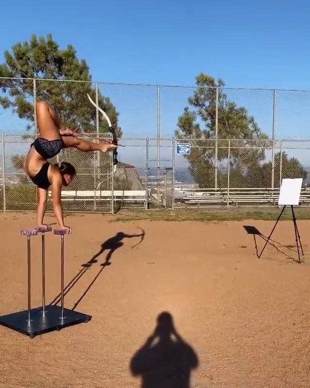 Woman Does Handstand and Shoots Bow Shot via Toes