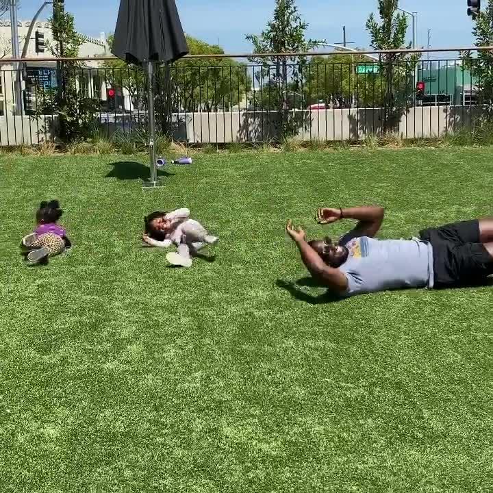Man Plays With his Kids by Rolling Down on Grass Slope With Them